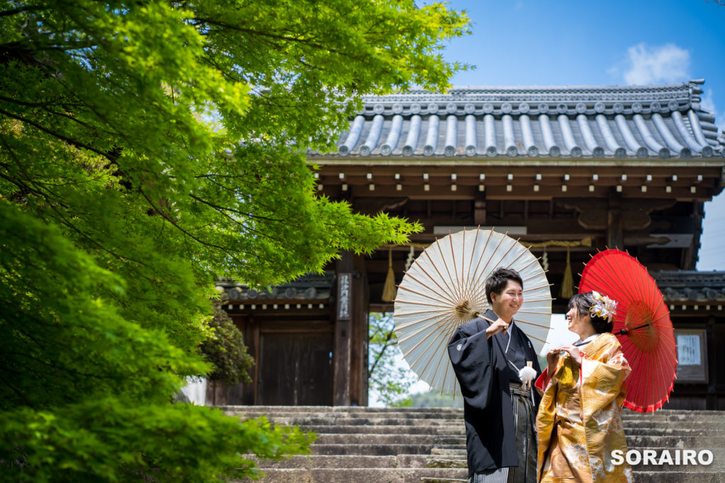 お寺の門をバックに番傘を持つ和装姿の男女